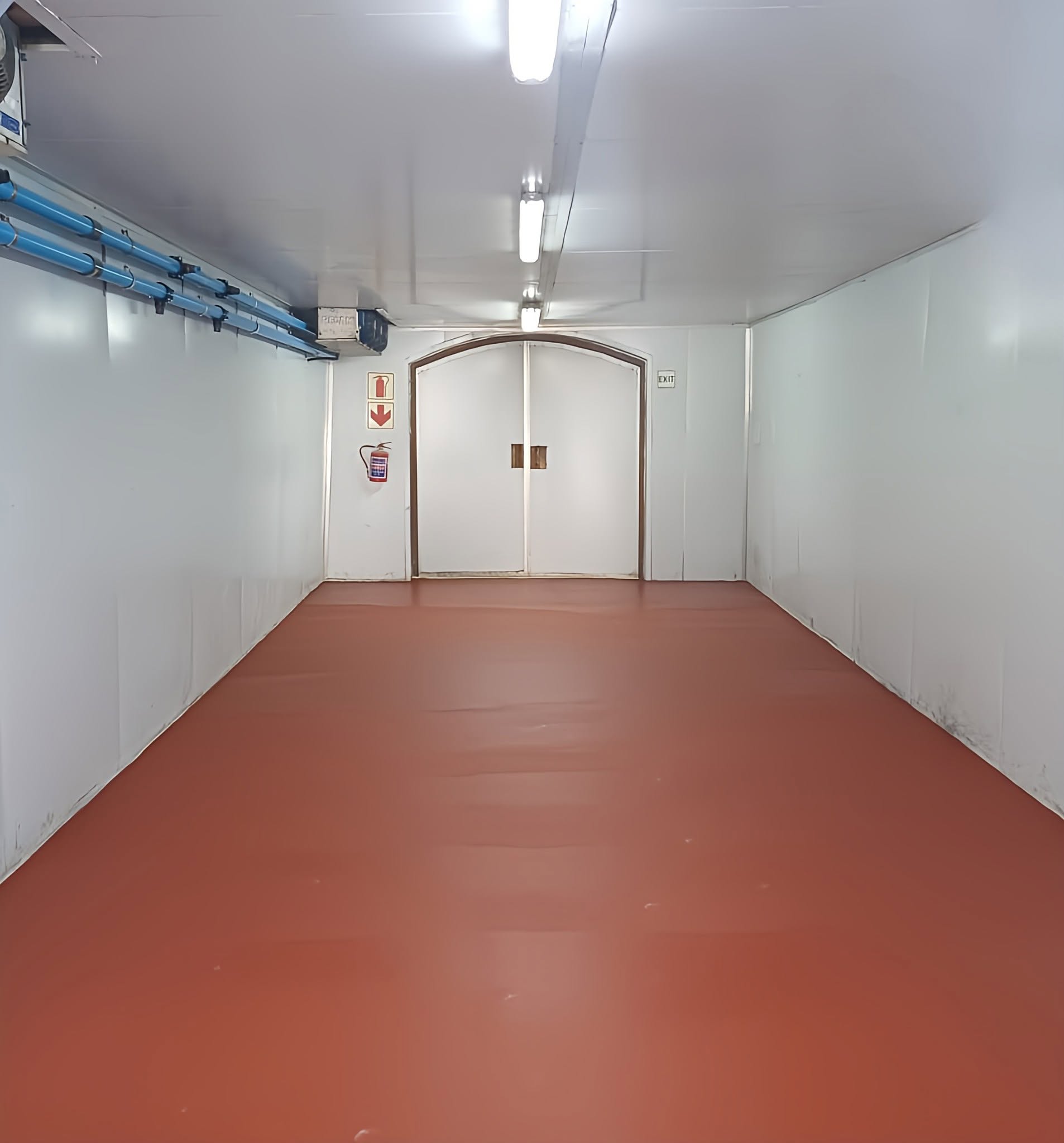 Glossy terracotta-red epoxy resin floor with coved skirting in a commercial storage room