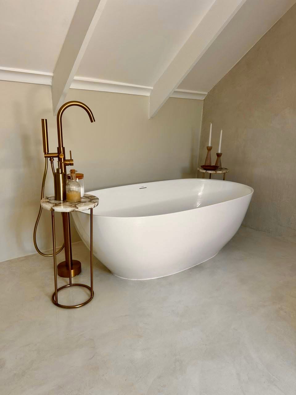 Freestanding bathtub on a seamless microcement floor with matching microcement walls and brass fittings