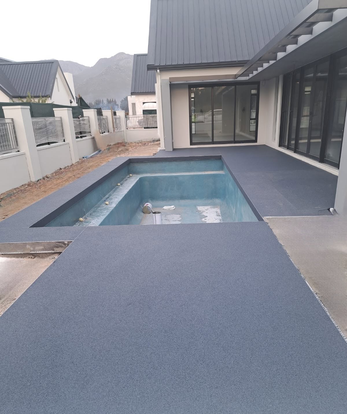 Dark grey stone carpet pool surround and patio finish outside a modern house